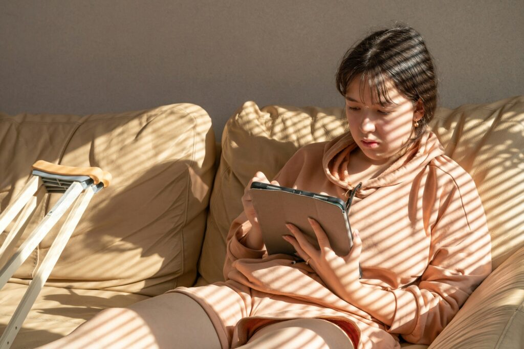 Girl with a cast on their leg, sitting on the couch and drawing on a graphics tablet.